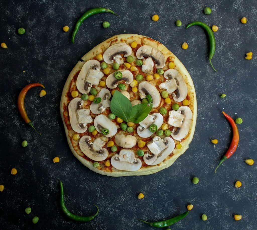 Frisch gebackene Pizza mit Champignons, Erbsen und Mais als vegetarische Variante auf einem Holzbrett serviert