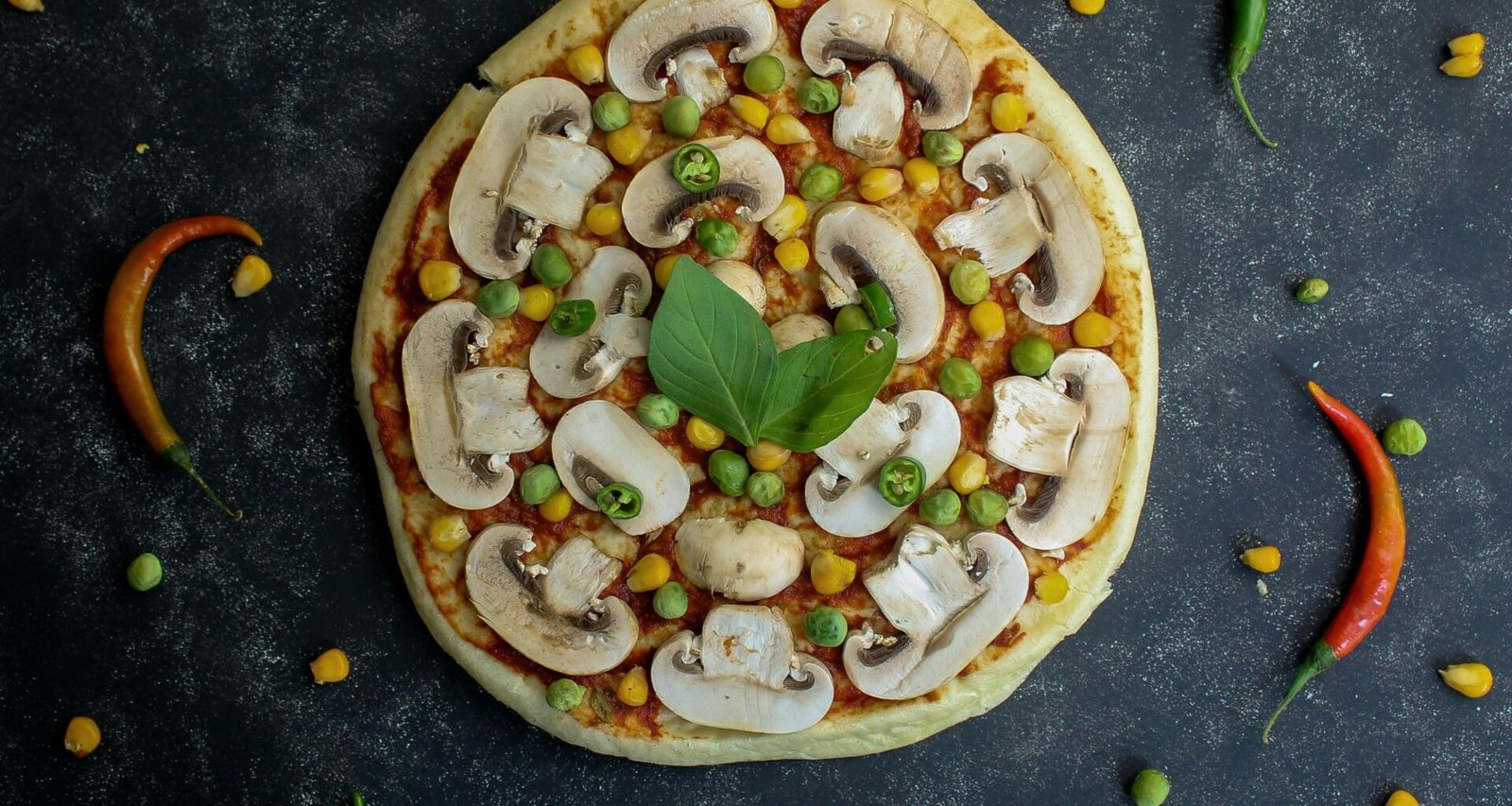 Frisch gebackene Pizza mit Champignons, Erbsen und Mais als vegetarische Variante auf einem Holzbrett serviert