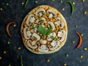 Frisch gebackene Pizza mit Champignons, Erbsen und Mais als vegetarische Variante auf einem Holzbrett serviert