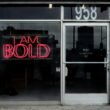 Rotes Neon-Leuchtschild mit der Aufschrift „I am bold“ an einer dunklen Wand, fotografiert von Max Böhme