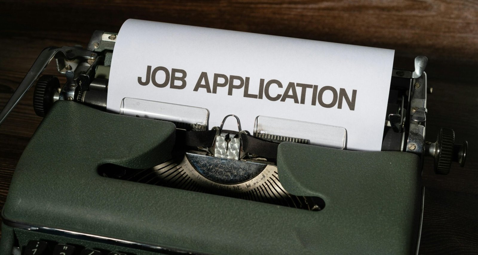 Eine schwarze Schreibmaschine mit einer gedruckten Bewerbung auf weißem Papier, fotografiert auf einem Holztisch
