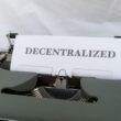 Schreibmaschine mit eingelegtem Papier, auf dem das Wort decentralized steht. Symbolbild für Dezentralisierung und Technologie.