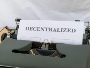 Schreibmaschine mit eingelegtem Papier, auf dem das Wort decentralized steht. Symbolbild für Dezentralisierung und Technologie.