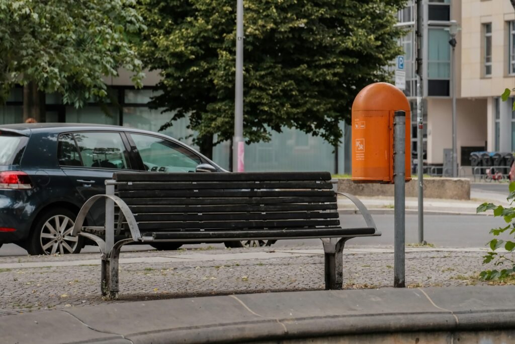 Schwarze Bank am Straßenrand mit Asphalt und Gehweg, urbanes Straßenbild, klare Linien und offene Umgebung