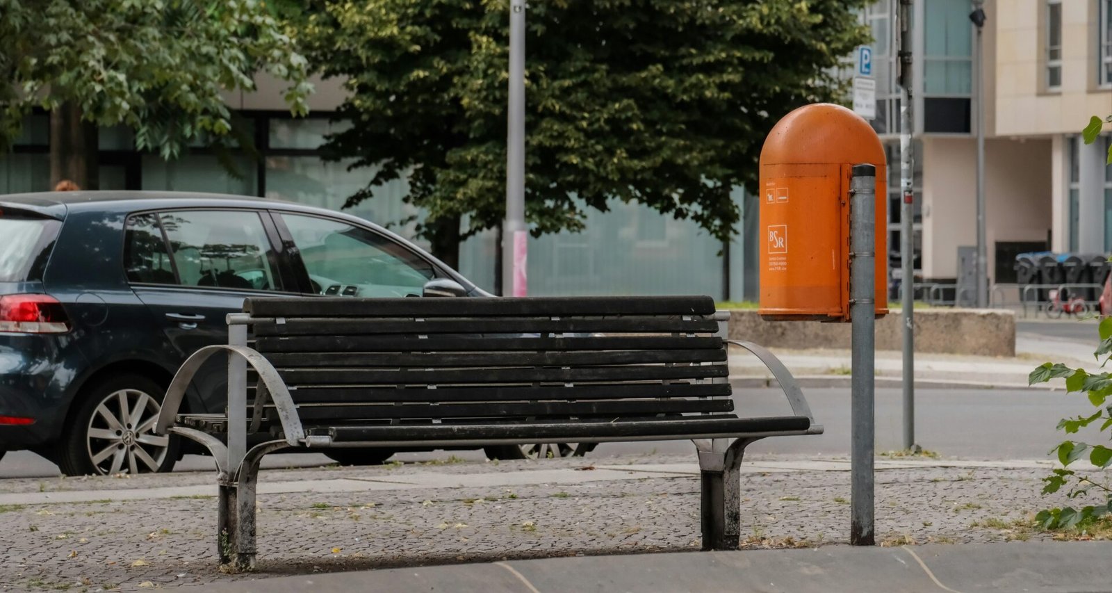 Schwarze Bank am Straßenrand mit Asphalt und Gehweg, urbanes Straßenbild, klare Linien und offene Umgebung