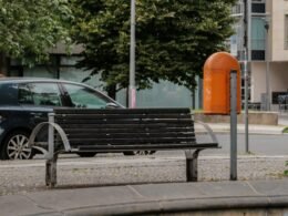 Schwarze Bank am Straßenrand mit Asphalt und Gehweg, urbanes Straßenbild, klare Linien und offene Umgebung