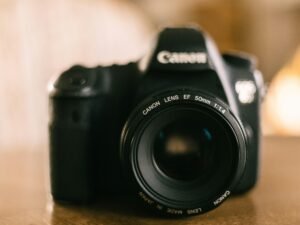 Eine schwarze Kamera steht auf einem hölzernen Tisch. Die Aufnahme zeigt moderne Technik in einer ruhigen Umgebung.