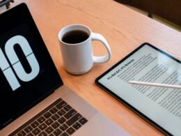 Ein Tablet und eine Kaffeetasse stehen nebeneinander auf einem Holztisch in entspannter Arbeitsatmosphäre.