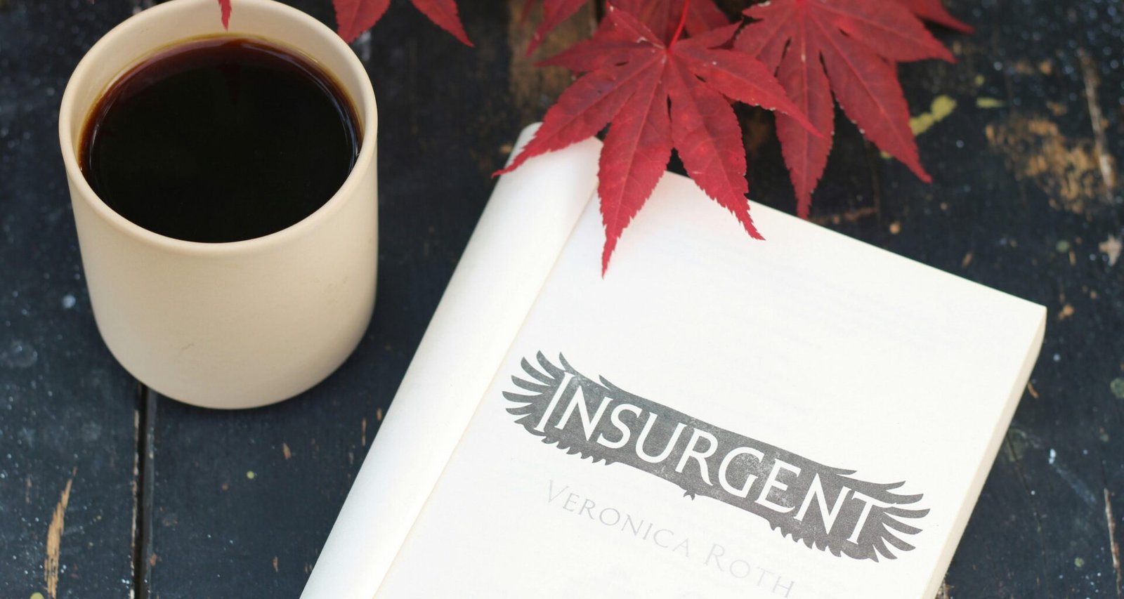 Eine Tasse Kaffee neben einem aufgeschlagenen Buch steht auf einem Holztisch in hellem Tageslicht.