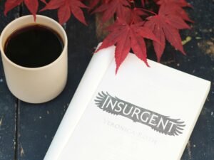 Eine Tasse Kaffee neben einem aufgeschlagenen Buch steht auf einem Holztisch in hellem Tageslicht.