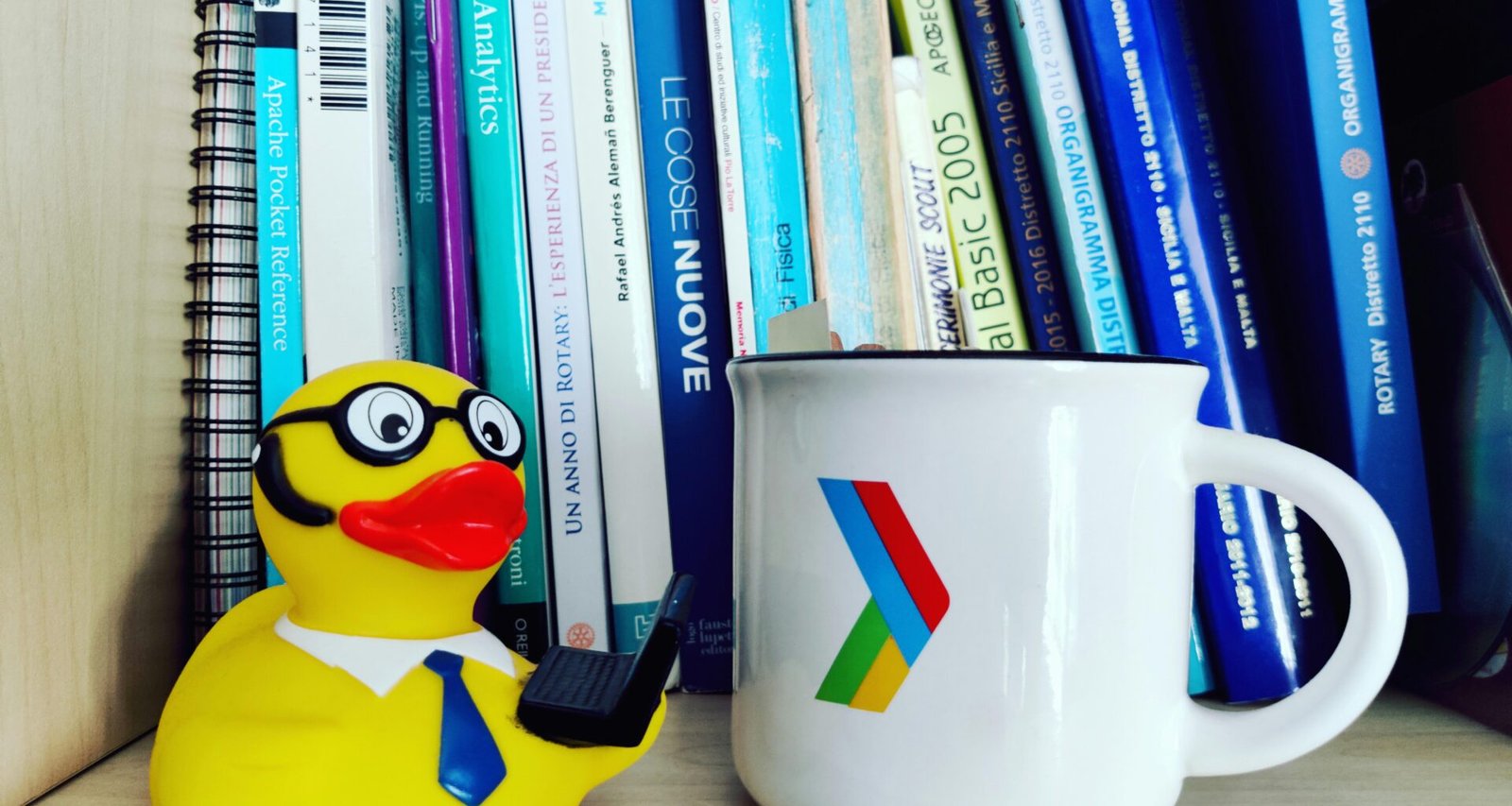 Eine weiße Kaffeetasse steht neben einem Stapel Bücher auf einem Holztisch, umgeben von natürlichem Licht.