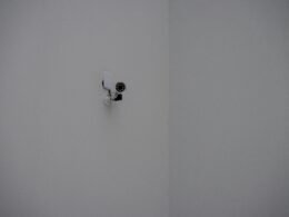 Weiße Sicherheitskamera an einer schlichten Gebäudeecke montiert und auf den Innenraum ausgerichtet