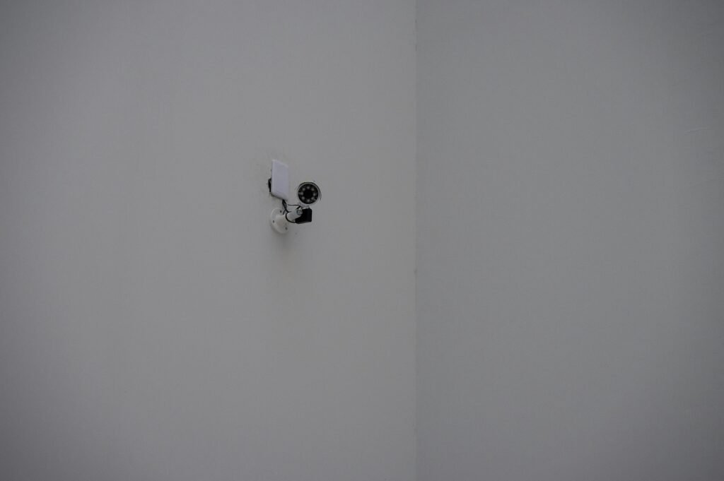 Eine Sicherheitskamera ist an der Ecke eines weißen Gebäudes montiert und fokussiert auf den Überwachungsbereich.