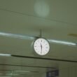 Große analoge Uhr hängt von der Decke in einem modernen Flughafen und zeigt Reisenden die aktuelle Uhrzeit.