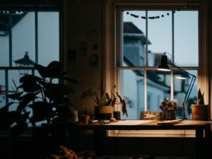 Ein Blumenstrauß in einer Vase steht auf einem Tisch direkt neben einem großen Fenster in einem hellen Raum.