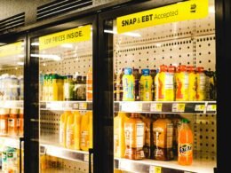 Ein Kühlregal in einem Supermarkt, das mit mehreren Flaschen Orangensaft sorgfältig bestückt ist.