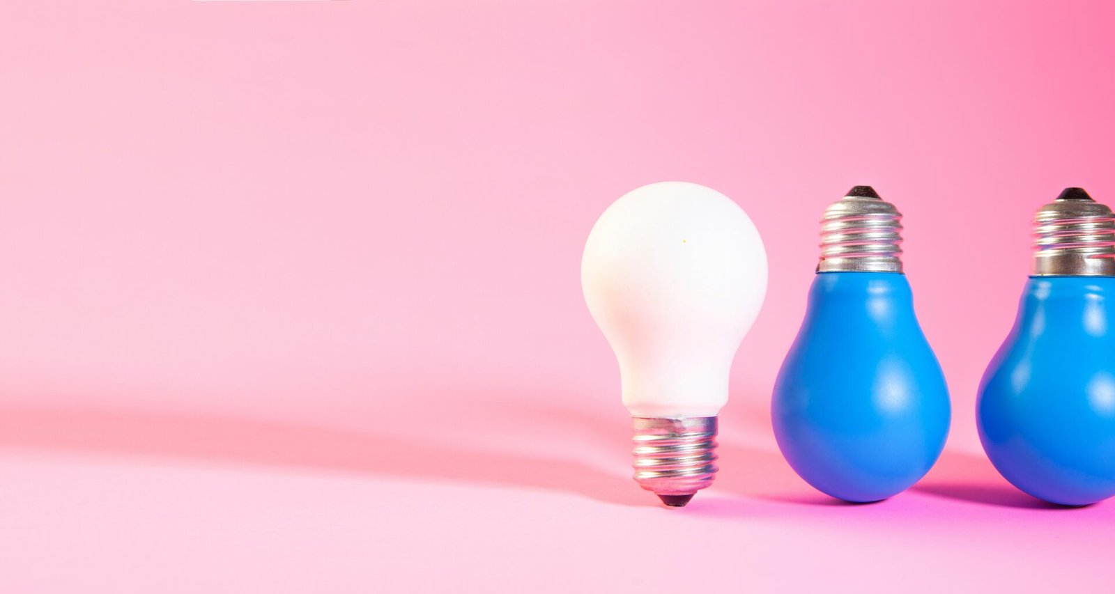 Eine weiße Glühbirne steht zwischen zwei blauen Glühbirnen auf hellem Untergrund. Foto von Sasun Bughdaryan.