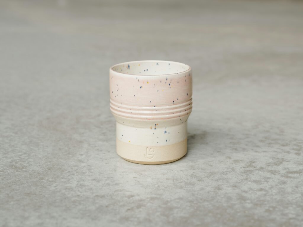 Weiße Kaffeetasse steht auf einer grauen Oberfläche in minimalistischem Stil, fotografiert bei natürlichem Licht.