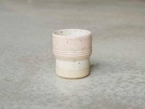 Weiße Kaffeetasse steht auf einer grauen Oberfläche in minimalistischem Stil, fotografiert bei natürlichem Licht.