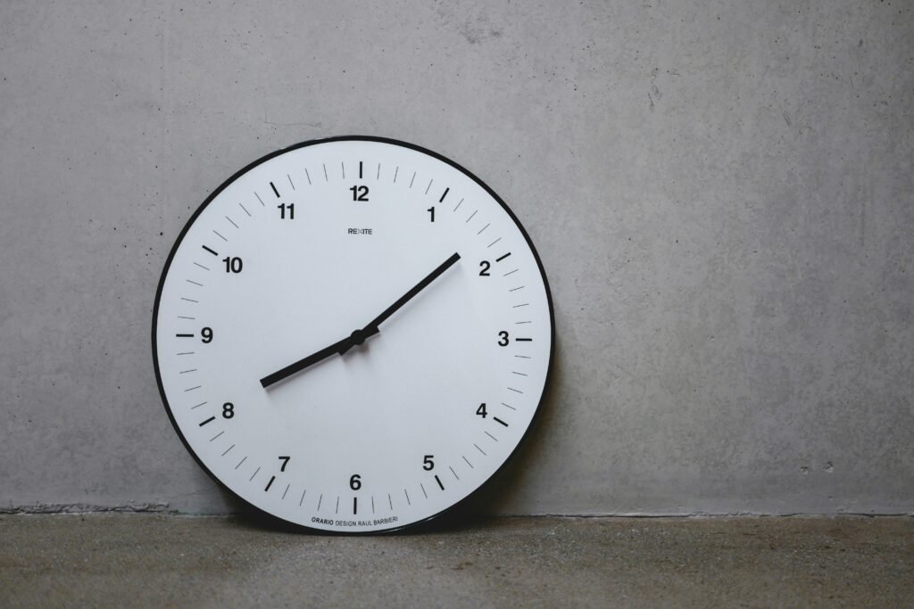 Weiße Wanduhr mit schwarzem Sekundenzeiger an einer neutralen Wand als Symbol für Zeitmanagement und Organisation.