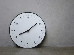 Weiße Wanduhr mit schwarzem Sekundenzeiger an einer neutralen Wand als Symbol für Zeitmanagement und Organisation.