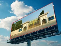 Ein großes Billboard zeigt das Foto eines Gebäudes und steht in einer städtischen Umgebung neben weiteren Bauwerken.