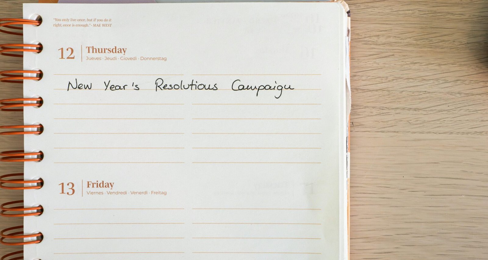 Notizbuch mit handschriftlicher Aufschrift ‚new year's resolution campaign‘ auf weißem Tisch, geeignet für Marketing-Artikel