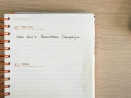 Notizbuch mit handschriftlicher Aufschrift ‚new year's resolution campaign‘ auf weißem Tisch, geeignet für Marketing-Artikel