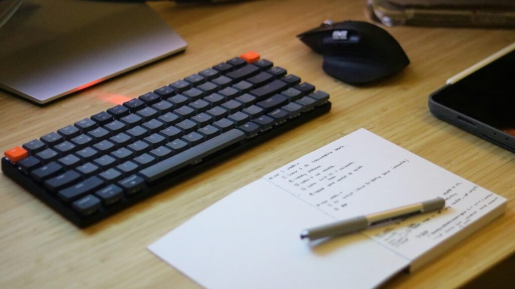 Ein Schreibtisch mit Computer-Tastatur, Maus, Smartphone und Notizblock, perfekt für digitale Arbeitsumgebungen arrangiert.