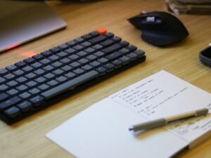 Ein Schreibtisch mit Computer-Tastatur, Maus, Smartphone und Notizblock, perfekt für digitale Arbeitsumgebungen arrangiert.