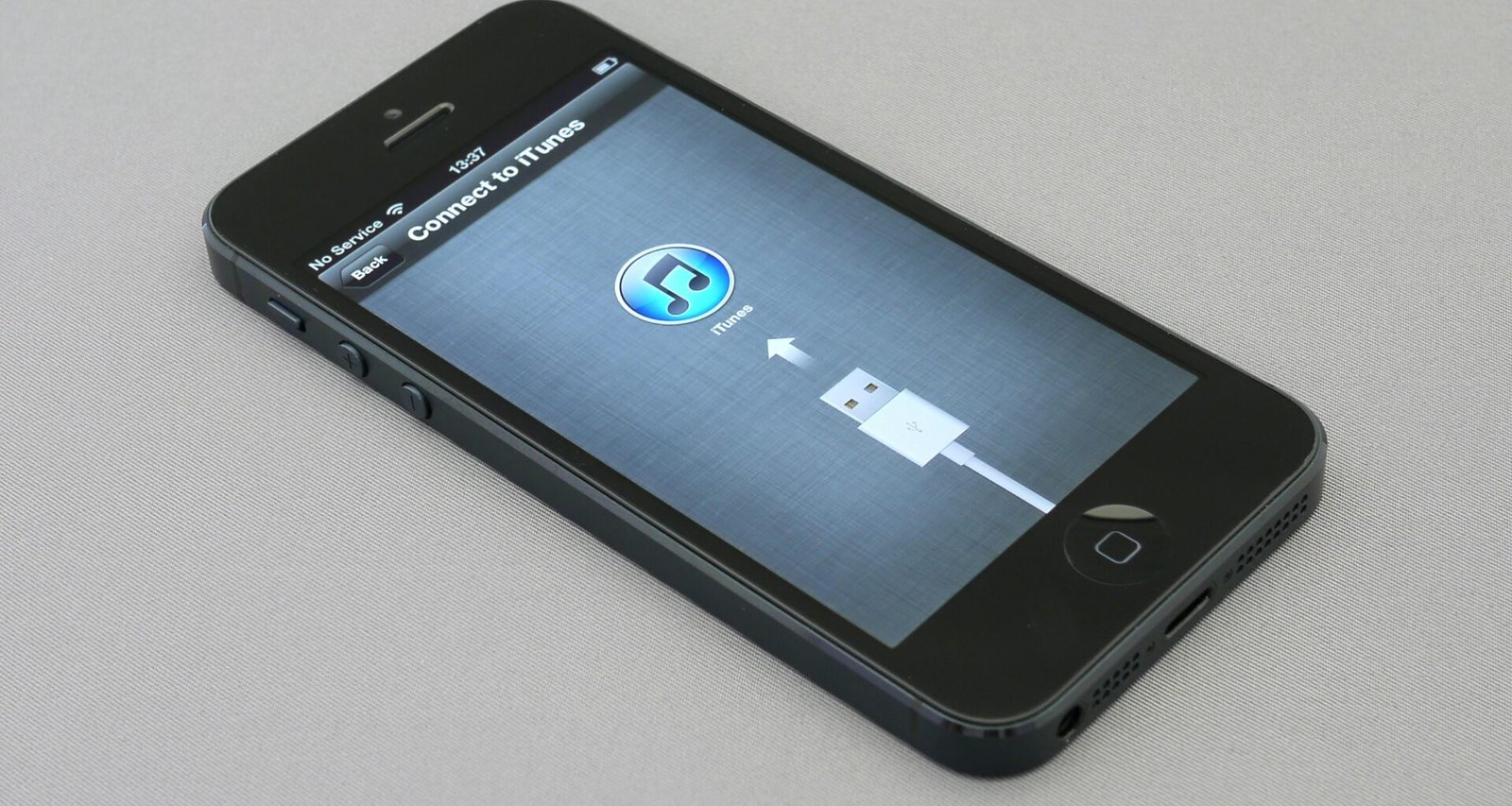 Ein eingeschaltetes iPhone 5 liegt auf einer hellen Oberfläche und zeigt den Homebildschirm mit App-Symbolen.