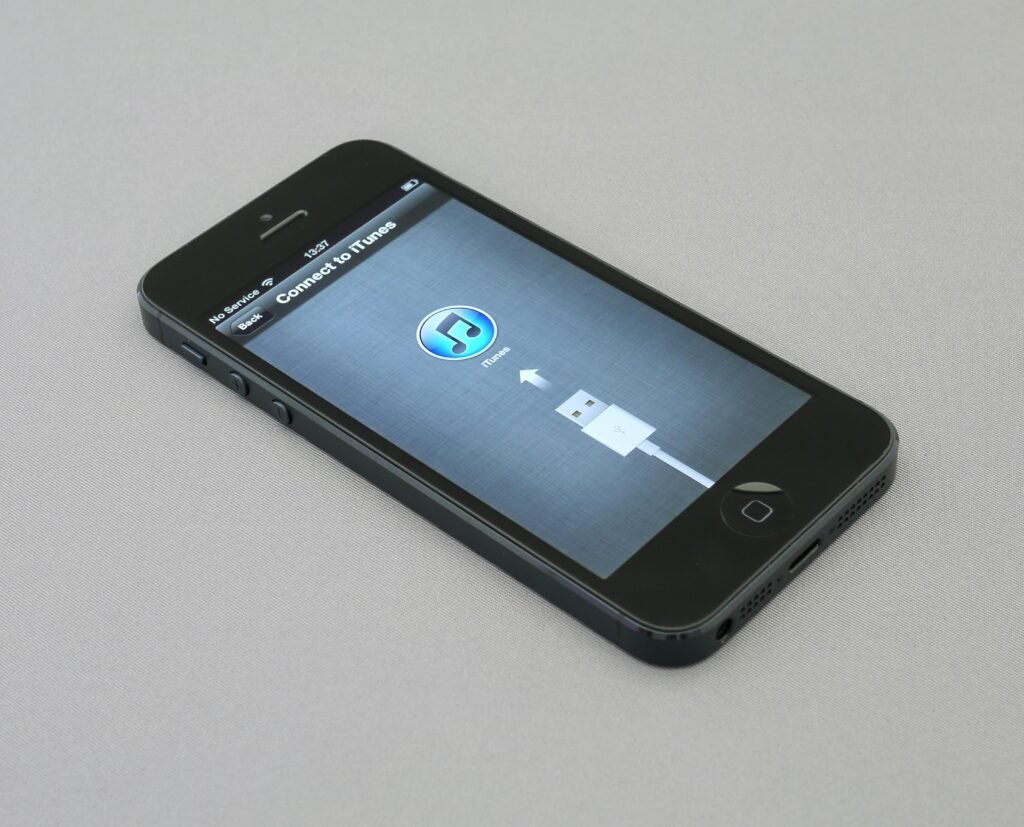 Ein eingeschaltetes iPhone 5 liegt auf einer dunklen Oberfläche und zeigt den Startbildschirm deutlich.