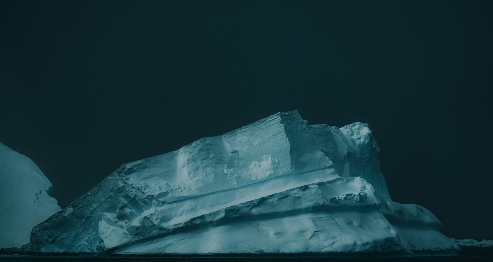 Ein großer Eisberg schwimmt auf dunklem Wasser unter bewölktem Himmel. Foto von Matthew Stephenson.