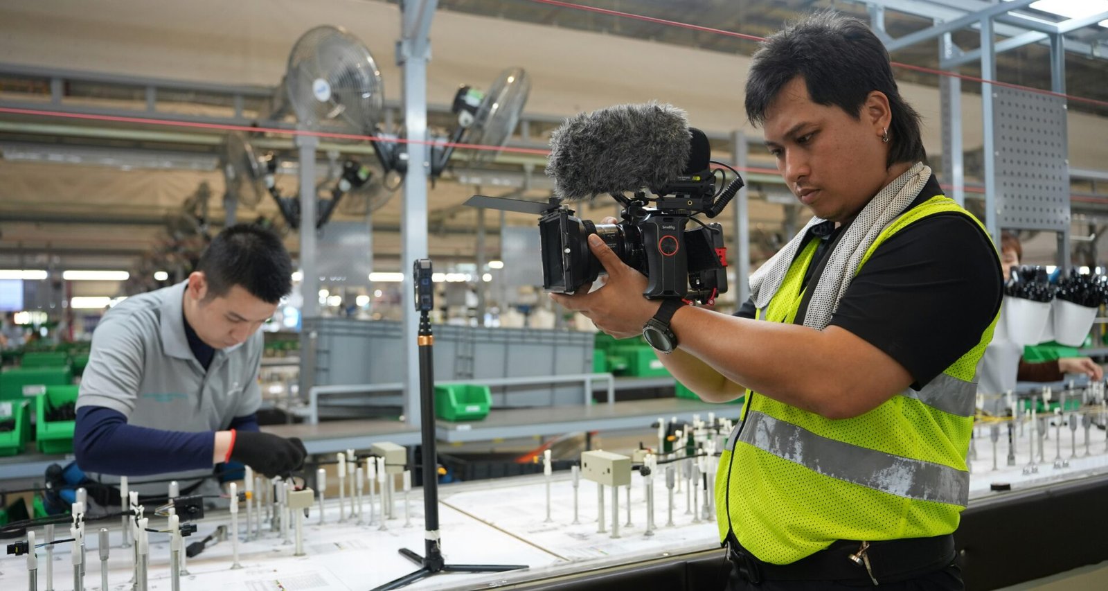 Ein Filmemacher filmt Mitarbeitende an einer automatisierten Produktionslinie in einer modernen Fabrikhalle