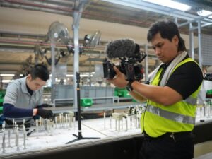 Ein Filmemacher filmt Mitarbeitende an einer automatisierten Produktionslinie in einer modernen Fabrikhalle