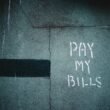 Schriftzug „Pay My Bills“ als Graffiti auf einer Wand, unscharf fotografiert und als Symbol urbaner Street-Art dargestellt
