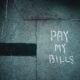 Schriftzug „Pay My Bills“ als Graffiti auf einer Wand, unscharf fotografiert und als Symbol urbaner Street-Art dargestellt