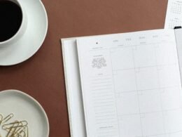 Flatlay mit aufgeschlagenem Buch und einer weißen Tasse Tee auf einem hellen Sofa