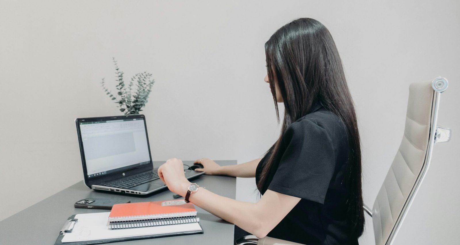 Frau sitzt an einem Schreibtisch und arbeitet mit einem Laptop, umgeben von Notizbüchern und Arbeitsmaterialien