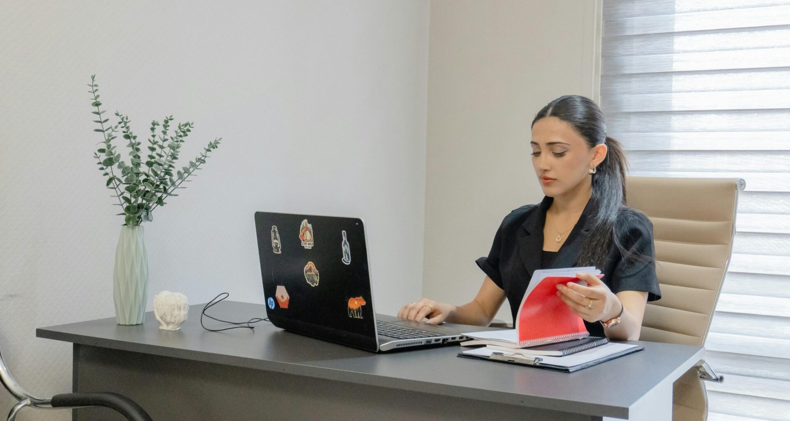 Frau arbeitet an einem Schreibtisch mit Laptop, umgeben von Notizbuch und Stift, in einem modernen Büro