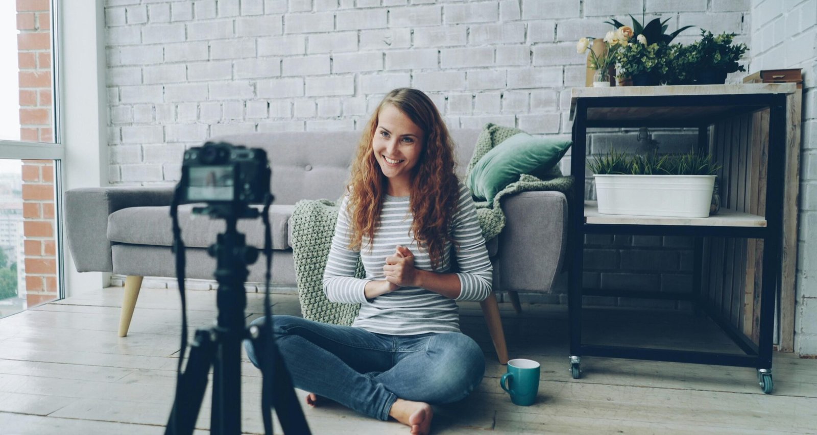 Frau sitzt auf dem Fußboden und filmt sich selbst mit einer Kamera; ideal illustriert für Artikel über Content-Erstellung
