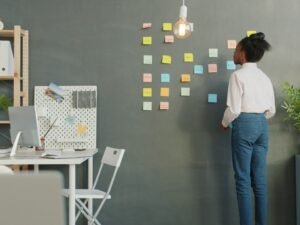 Eine Frau klebt verschiedene bunte Haftnotizen an eine Wand, um Ideen für ein Teamprojekt zu organisieren.