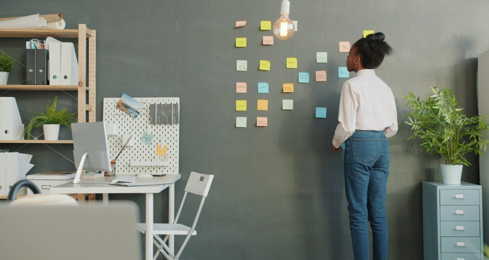Frau befestigt verschiedenfarbige Haftnotizen an einer weißen Wand bei einem Teamworkshop oder Meeting.