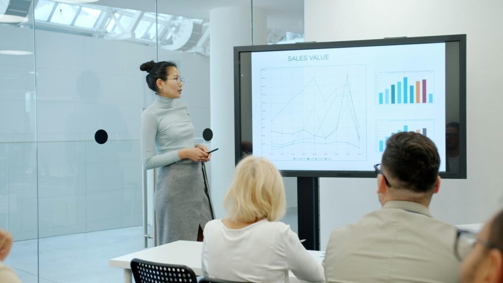 Frau steht vor einer Gruppe und zeigt auf ein Diagramm während einer Geschäfts- oder Marketingpräsentation.