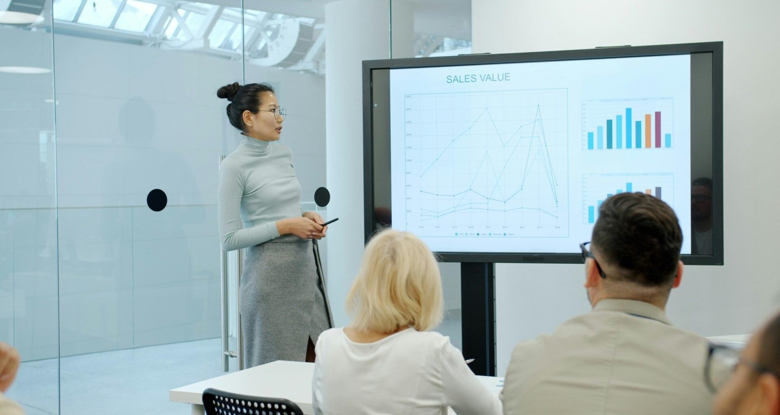 Frau steht vor einer Gruppe und zeigt auf ein Diagramm während einer Geschäfts- oder Marketingpräsentation.