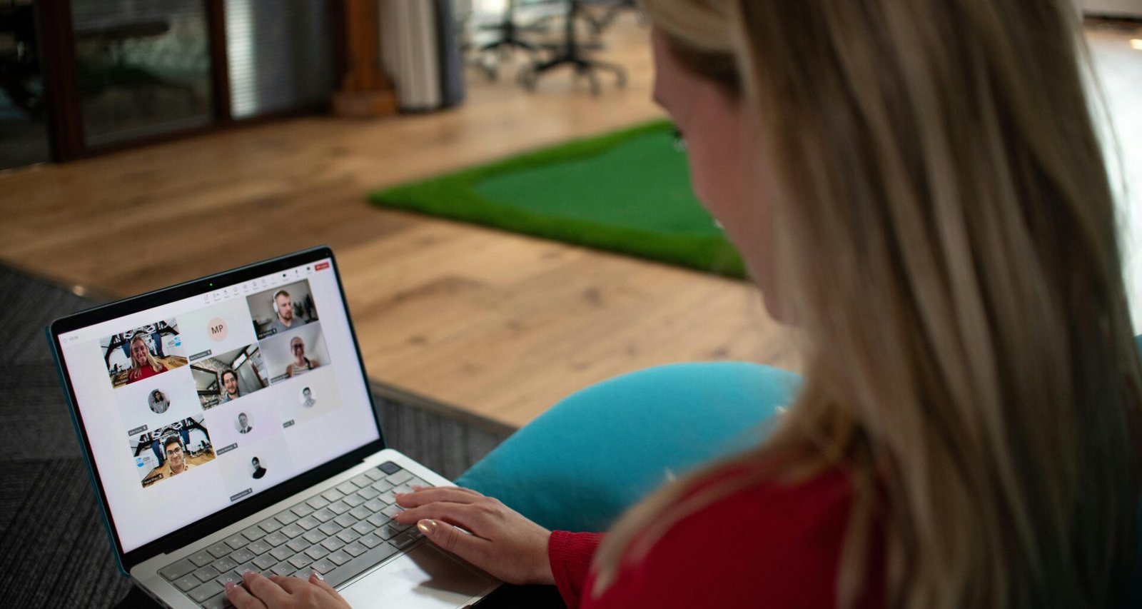 Frau sitzt am Schreibtisch und nimmt an einer Videokonferenz auf dem Laptop teil, mehrere Teilnehmer sind auf dem Bildschirm sichtbar.