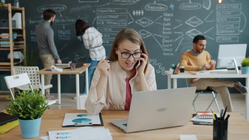 Frau sitzt am Schreibtisch, telefoniert und jubelt über einen beruflichen Erfolg während eines Business-Calls.