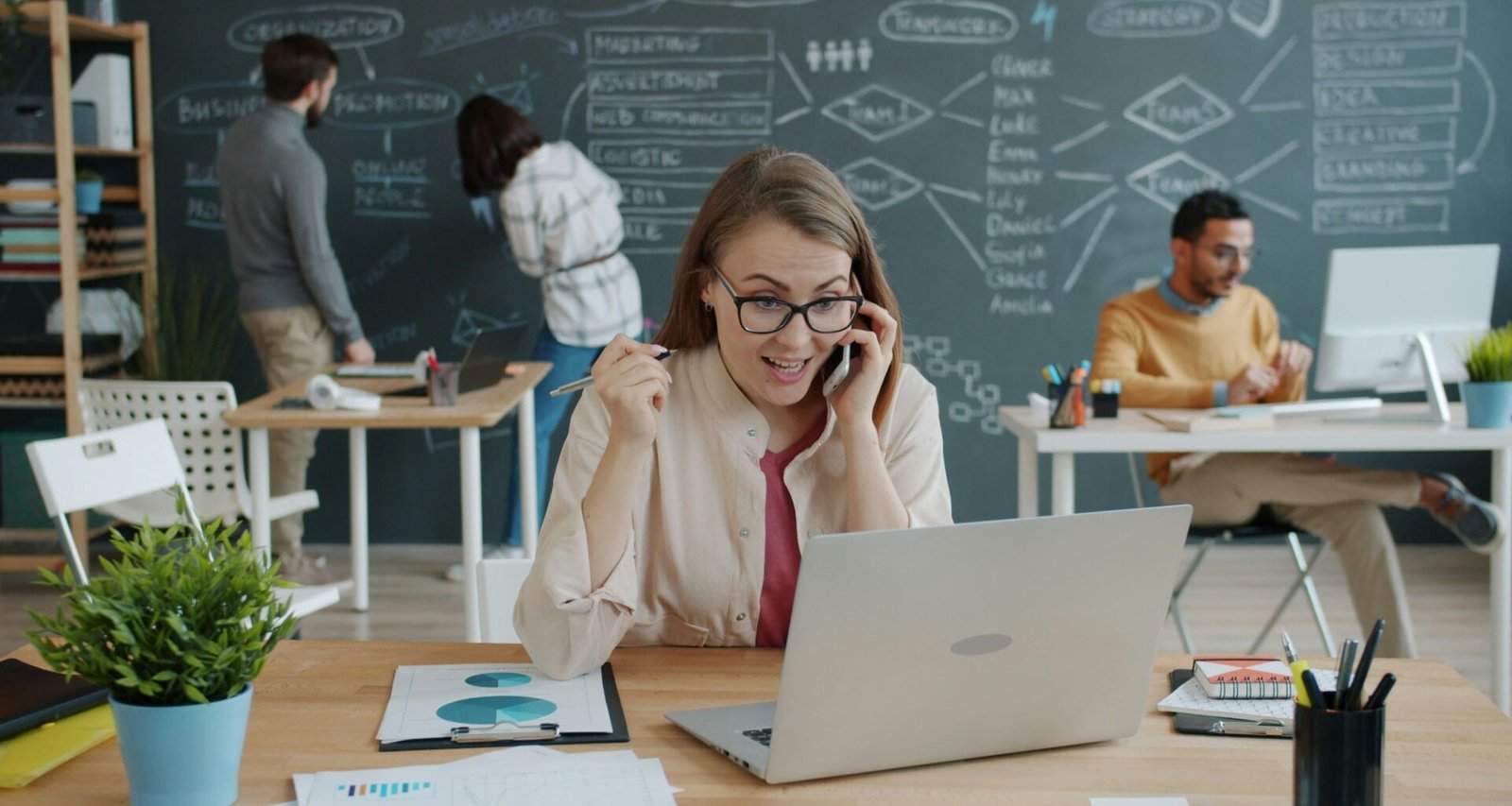 Frau sitzt am Schreibtisch, telefoniert und jubelt über einen beruflichen Erfolg während eines Business-Calls.