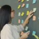 Frau platziert bunte Sticky Notes auf einer dunklen Wand als Teil eines kreativen Arbeitsprozesses im Büro.