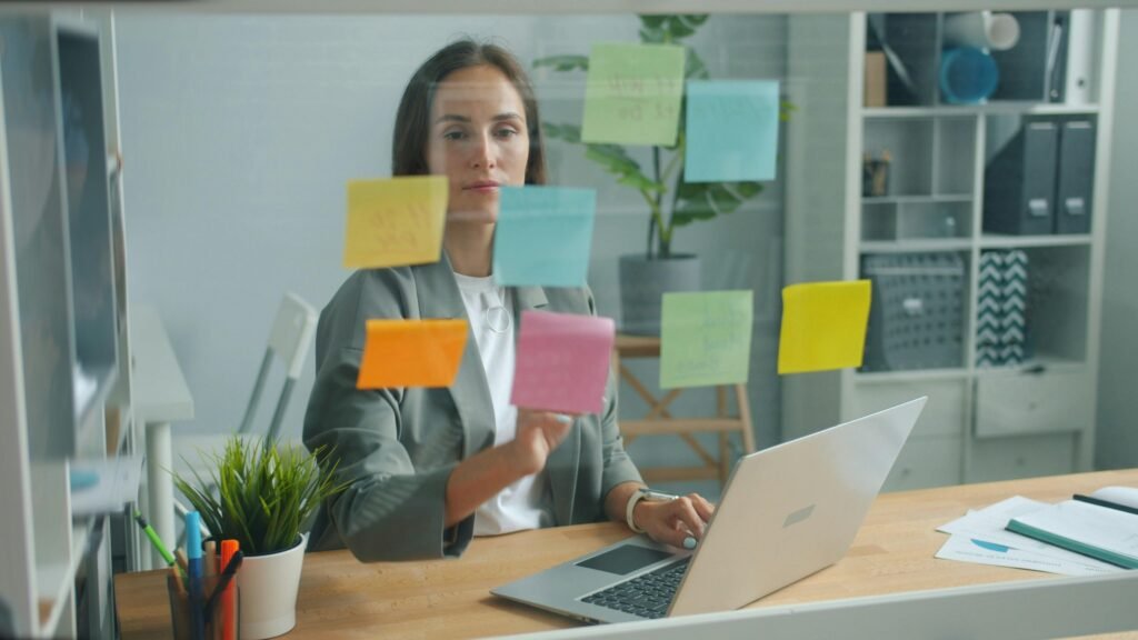 Frau ordnet bunte Haftnotizen auf einer Glaswand für Brainstorming und Projektplanung im modernen Büro.